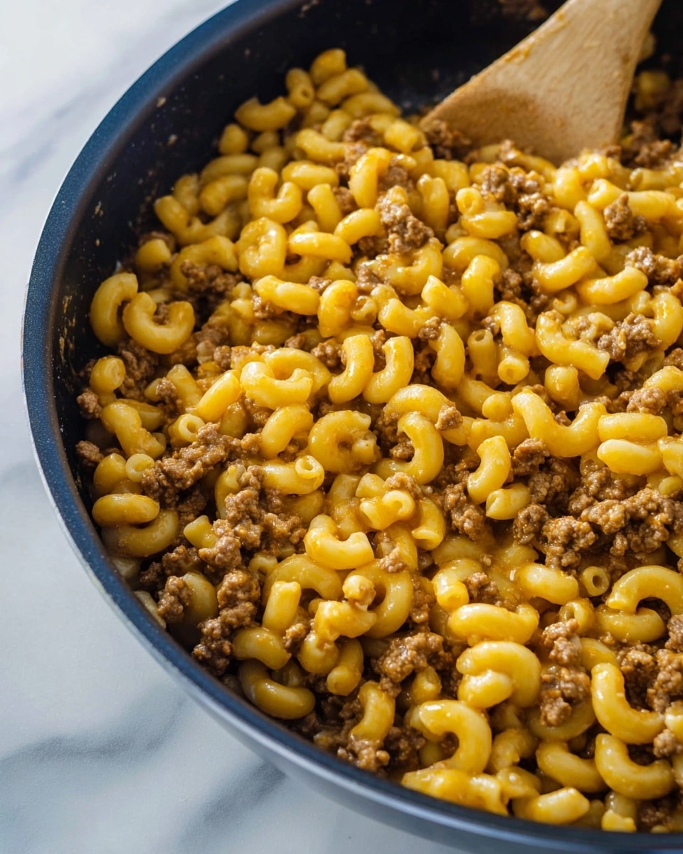 The image shows a white bowl filled with creamy macaroni and ground meat. The dish has three layers visible: the bottom layer is soft elbow macaroni with a smooth yellow cheese sauce coating it, the middle layer is browned ground meat scattered throughout the macaroni, and the top layer is fresh green parsley leaves sprinkled over the pasta. The bowl sits on a white marbled surface, and a spoon is partially visible in the bowl, ready to scoop the food. In the background, part of a pan with more macaroni is seen out of focus. photo taken with an iphone --ar 4:5 --v 7