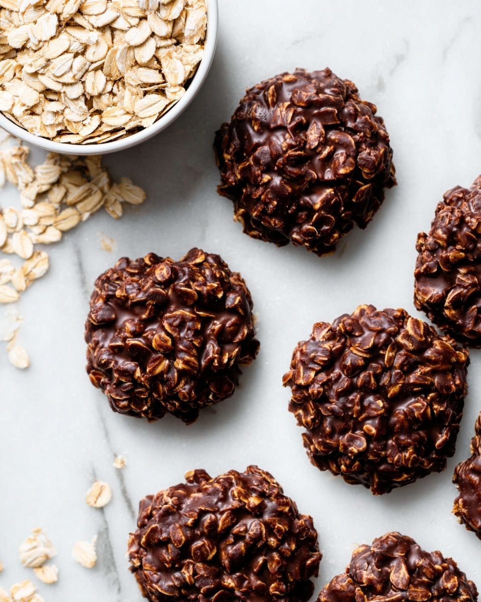 The image shows several no-bake chocolate oat cookies scattered on a white marbled surface. Each cookie is a single thick layer, dark brown from the chocolate, with visible rolled oats embedded throughout, giving a rough texture. The cookies are irregular in shape but generally round and clumped, with a shiny, slightly glossy look from the chocolate coating. In the top left corner, there is a white bowl filled with plain rolled oats, showing their pale tan color and flat, slightly curved shape. The overall scene is bright and clean. photo taken with an iphone --ar 4:5 --v 7