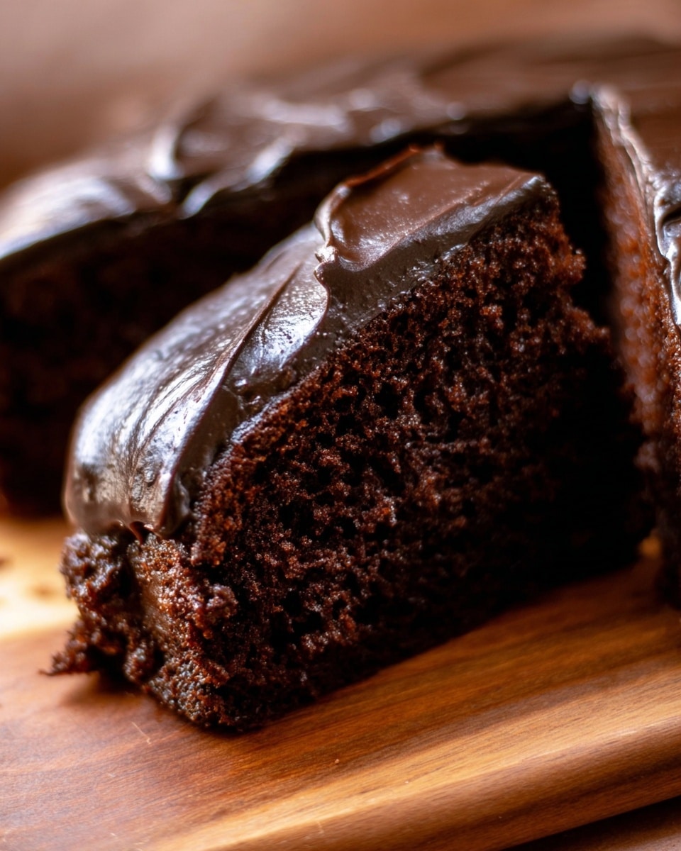 A rectangular chocolate loaf cake is placed on a wooden board with three thick slices cut in front. The cake has a rich dark brown color with a moist, dense texture inside. Each slice and the top of the whole loaf is covered with a thick, smooth layer of glossy dark chocolate frosting, giving it a shiny and creamy look. The knife with some chocolate frosting on it is resting on the left side of the board. A small blurry pumpkin can be seen in the background. photo taken with an iphone --ar 4:5 --v 7