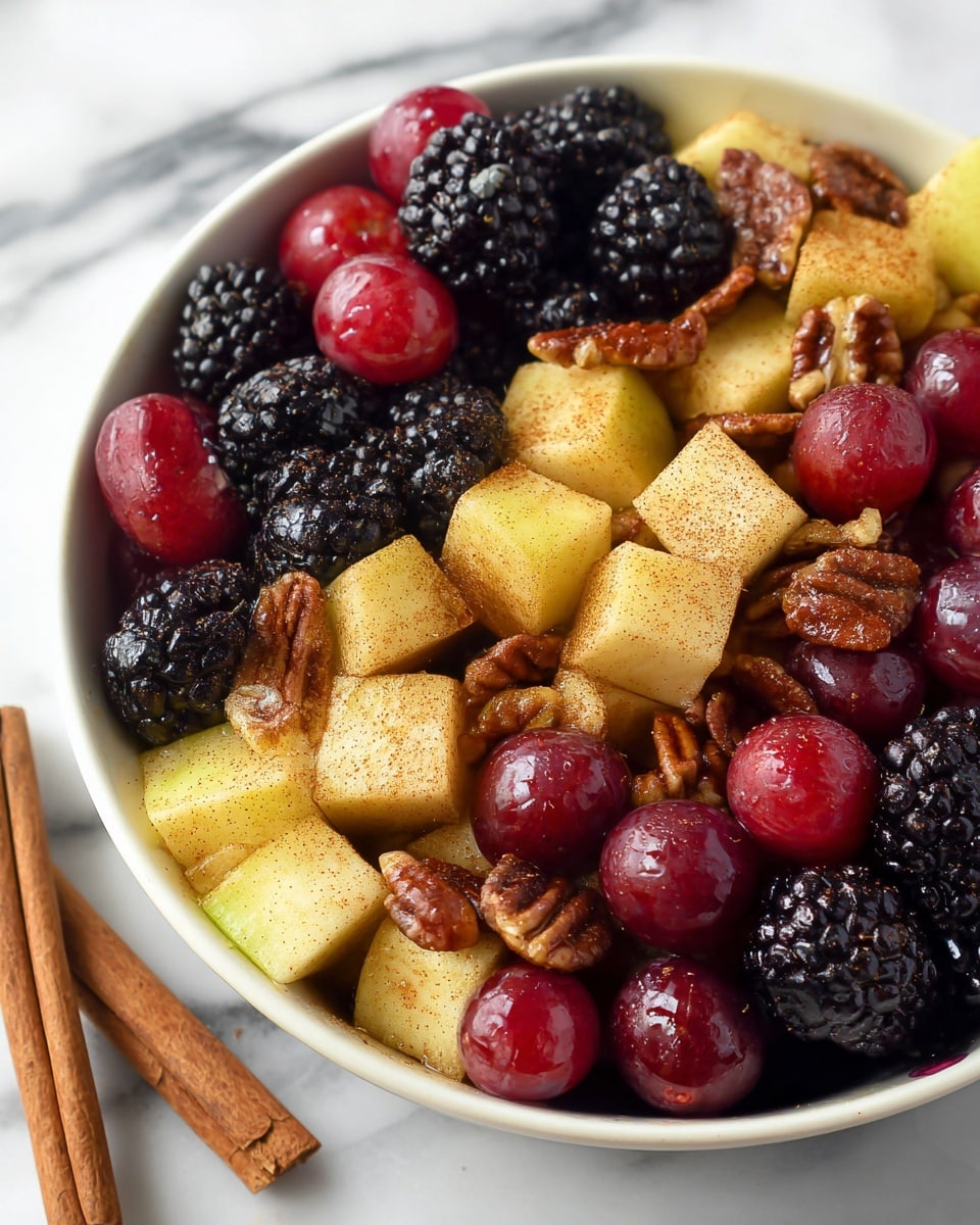 The image shows a close-up of a fruit salad in a white bowl filled with three main layers: the first layer is made up of glossy red grapes which look fresh and round; the second layer contains large, yellowish apple chunks coated with a light sprinkle of cinnamon giving them a slightly brown texture; the third layer features blackberries with a bumpy texture and rich dark purple color, scattered evenly throughout the bowl. Mixed within these layers are crunchy, brown pecan nuts adding texture and color contrast. The bowl sits on a white marbled surface with two cinnamon sticks placed beside it. photo taken with an iphone --ar 4:5 --v 7