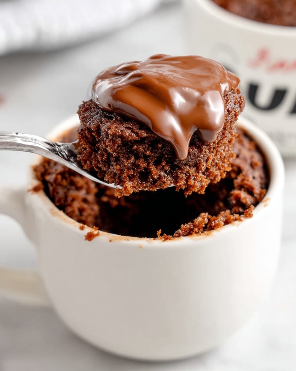 A white mug filled with a single, thick layer of dark brown chocolate cake with a moist and spongy texture, visible bubbles on the surface show its lightness; a silver spoon holds a portion of the cake above the mug, emphasizing the soft and airy inside. The mug rests on a cloth with a black and white grid pattern over a white marbled surface. Photo taken with an iphone --ar 4:5 --v 7