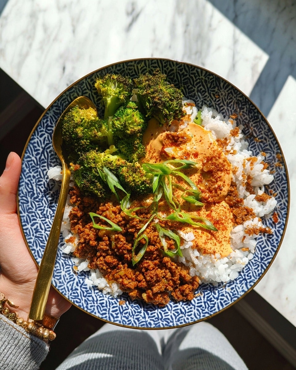 A white bowl with a blue geometric pattern holds a colorful dish. The bottom layer is fluffy white rice sprinkled with crispy light brown bits. On one side there are small green broccoli florets with a slight char. Next to the broccoli is a brown, crumbly textured cooked mixture, likely a spiced protein, with a few green onion slices scattered on top. In the center, there is a dollop of creamy orange sauce dusted with red seasoning. A gold spoon is placed near the brown mixture. A woman's hand holds the bowl over a white marbled surface, and sunlight casts sharp shadows. photo taken with an iphone --ar 4:5 --v 7