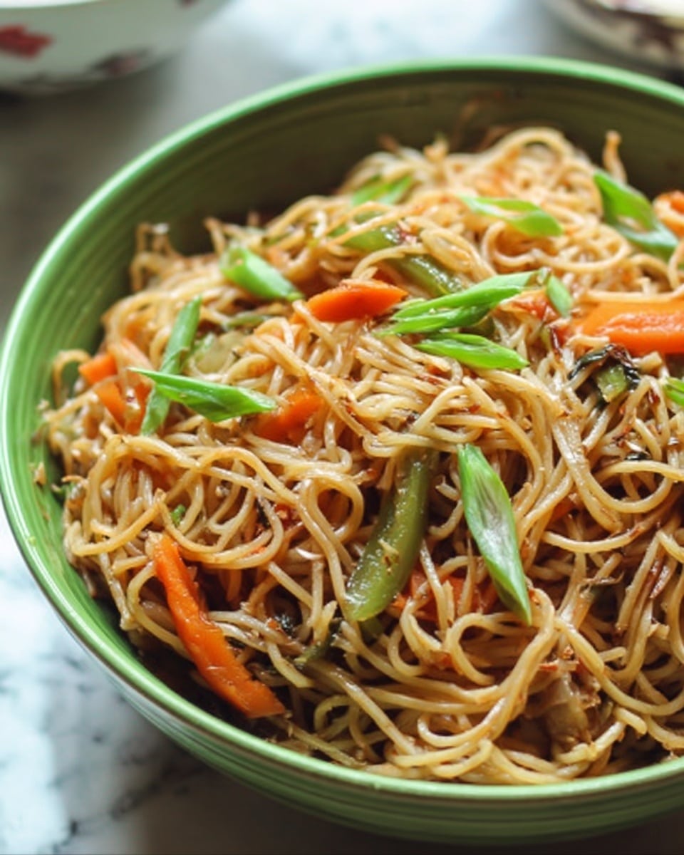 A close-up of a green bowl filled with stir-fried noodles mixed with small pieces of bright orange carrot slices, green peppers, and chopped green onions on top. The noodles are light brown with a glossy texture, tangled together showing soft and cooked strands. The bowl is placed on a white marbled surface with parts of a white bowl visible in the background. photo taken with an iphone --ar 4:5 --v 7