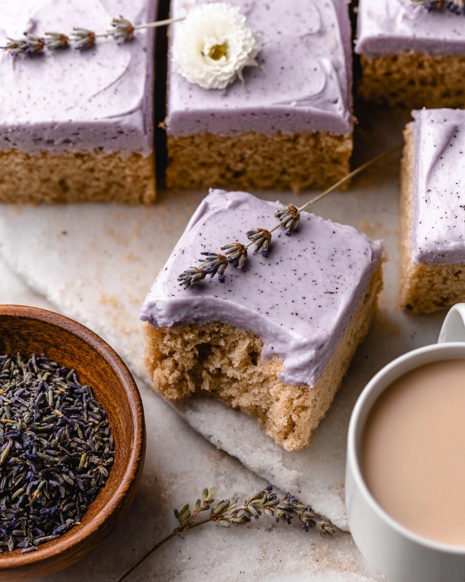 The image shows several square pieces of light brown cake with a thick layer of pale lavender frosting on top. The frosting is smooth with small dark specks and covers each piece evenly. One cake square is slightly lifted, showing the soft, crumbly texture of the cake underneath with a thin frosting layer on top. There is a small white flower and a sprig of dried lavender placed on one frosted cake piece. Near the cake, a wooden bowl holds dried lavender buds, and a white cup filled with a frothy light beige drink is partly visible. All items rest on a white marbled textured surface. photo taken with an iphone --ar 4:5 --v 7