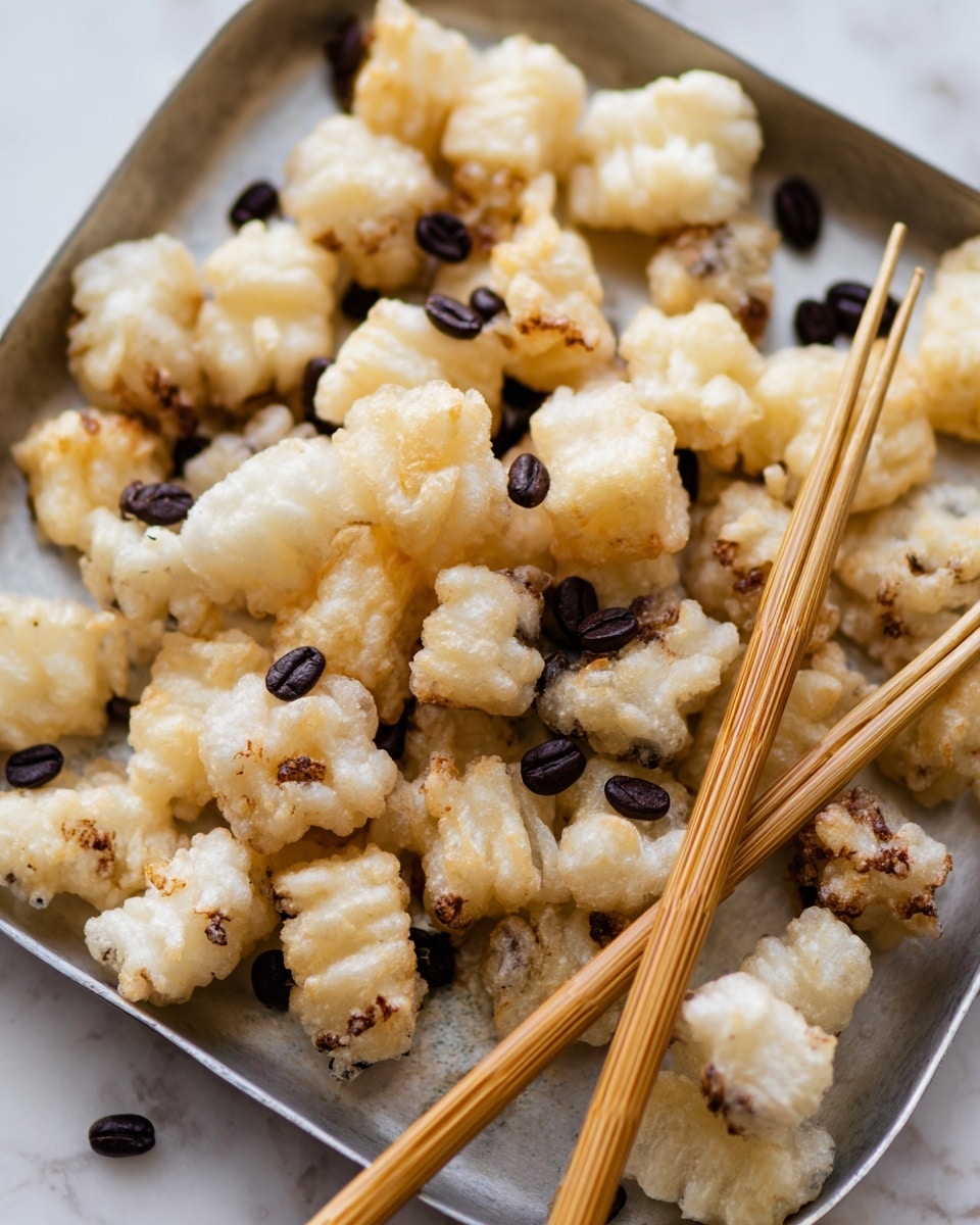 The image shows a metal tray filled with many small, unevenly shaped fried pieces that are pale golden and white, with some darker brown spots. The pieces have a crispy, textured surface with visible bubbles and irregular edges. Scattered over and between the pieces are small dark brown coffee beans adding contrast. A pair of light brown wooden chopsticks with ridges near the tips rests diagonally across the tray on top of the fried pieces. The tray is placed on a white marbled textured surface. photo taken with an iphone --ar 4:5 --v 7