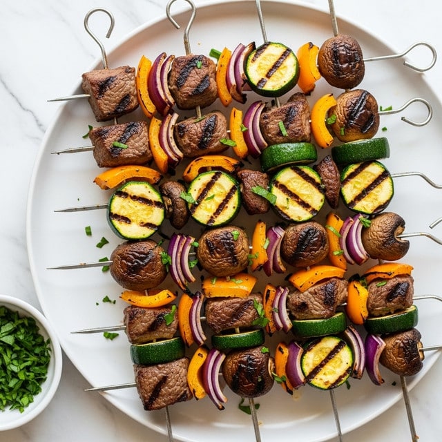 The image shows several metal skewers lying on a large white plate, each filled with colorful grilled ingredients. Each skewer has layers that repeat in this order from top to bottom: brown grilled beef cubes with a slightly charred texture, thick green slices of zucchini with grill marks, chunks of yellow and orange bell peppers, sections of purple-red onion, and whole dark brown mushrooms with a slightly wrinkled surface. The skewers are sprinkled with small pieces of fresh green herbs, adding a fresh touch. The plate sits on a white marbled surface, and there is a small white bowl filled with fresh chopped green herbs partly visible to the side. photo taken with an iphone --ar 4:5 --v 7