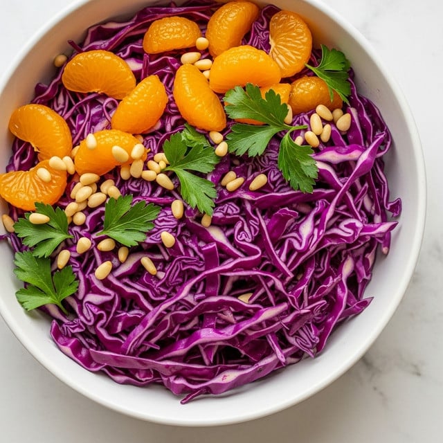 A white bowl filled with a colorful salad, showing three main layers: the bottom layer is bright purple shredded cabbage with its slightly shiny, fresh texture; scattered on top are small, shiny orange mandarin slices standing out with their smooth surface; the salad is finished with fresh green parsley leaves and small beige pine nuts sprinkled across. The bowl sits on a white marbled surface with soft natural light enhancing the vibrant colors of the salad. Photo taken with an iphone --ar 4:5 --v 7