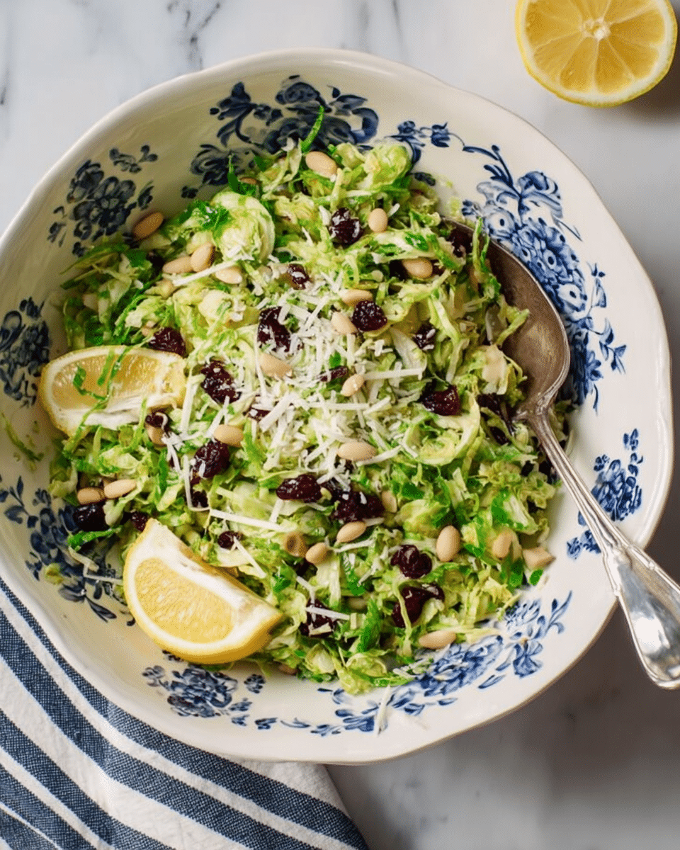 A large white bowl with blue floral patterns is filled with a fresh salad made of shredded green brussels sprouts as the main layer. Scattered on top are small dark purple dried cranberries, light beige pine nuts, and finely grated white cheese. Two thin lemon slices rest on one side of the salad near the edge of the bowl. A silver spoon is partially placed inside the bowl on the right side. The bowl sits on a white marbled surface with a navy and white striped cloth partially visible in the lower left corner. Photo taken with an iphone --ar 4:5 --v 7