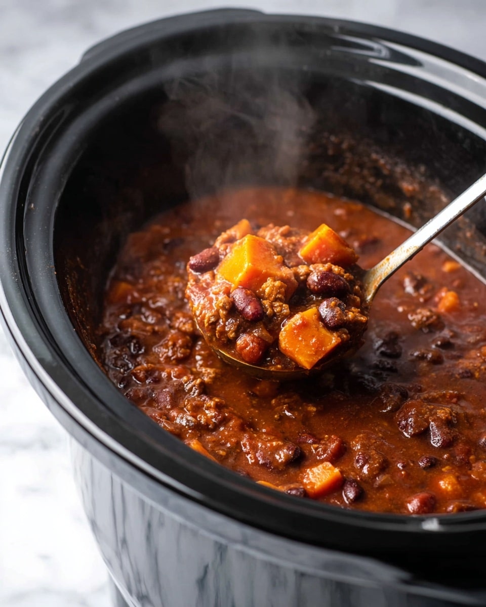 A close-up of a black slow cooker filled with thick, chunky chili showing visible pieces of orange sweet potato, dark brown beans, and tender meat in a rich, reddish-brown sauce, with steam rising from the pot. A metal ladle scoops a hearty portion of the chili, highlighting the textures of soft vegetables and beans coated in the thick sauce, all set on a white marbled surface. photo taken with an iphone --ar 4:5 --v 7