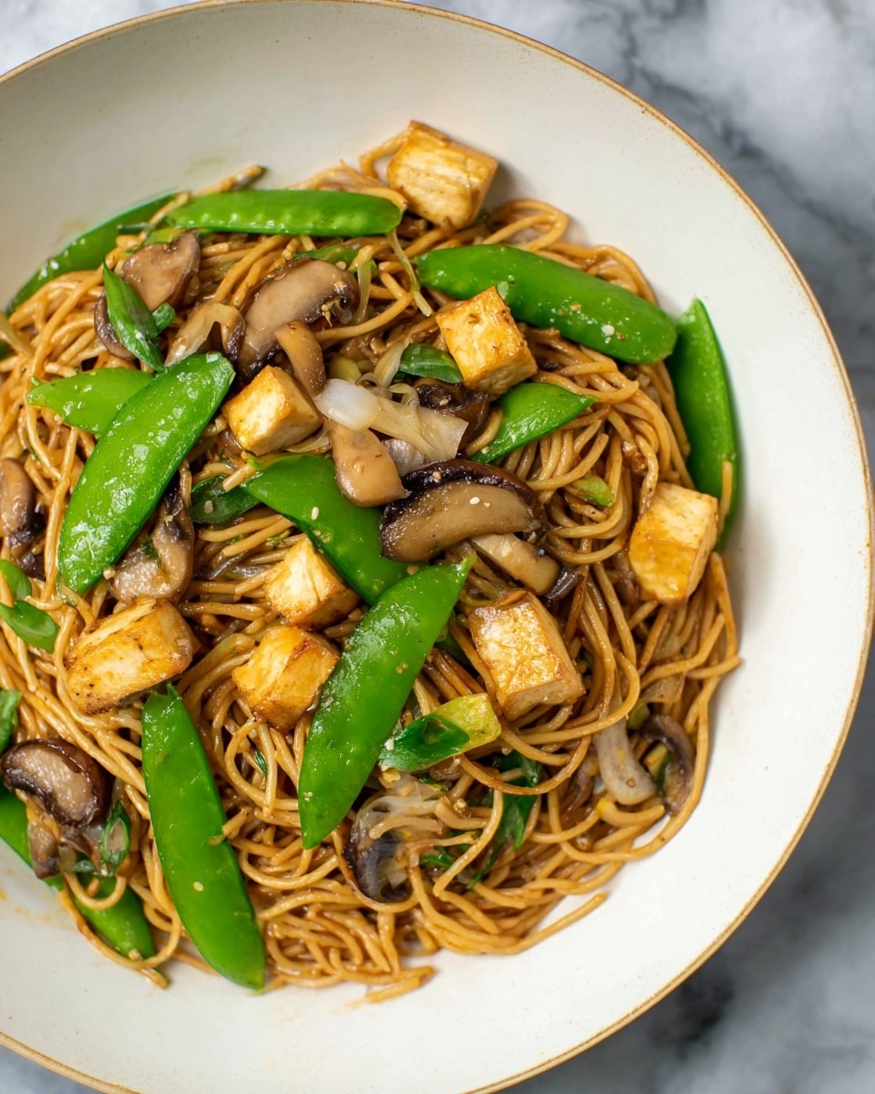 A white bowl filled with a serving of stir-fried noodles at the base, light brown and slightly shiny, layered with green snap peas and slices of brown mushrooms scattered on top. Small cubes of golden-brown tofu are evenly mixed throughout the noodles and vegetables, adding texture and color contrast. The dish sits on a white marbled surface, showing the details of each ingredient clearly. photo taken with an iphone --ar 4:5 --v 7