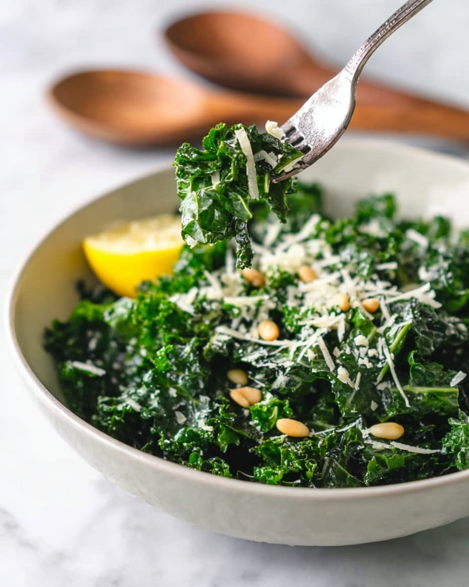 A bowl of fresh kale salad with three main layers: the base layer is dark green kale leaves with curly edges and a slightly shiny texture, the middle layer consists of small white shredded cheese sprinkled evenly across the kale, and the top layer has a few light brown pine nuts scattered on top. A metal fork is lifting some kale with cheese and pine nuts from the bowl, and there is a yellow lemon wedge nestled inside the bowl on the left side. The bowl is white, placed on a white marbled surface, with two wooden salad spoons blurred in the background. Photo taken with an iphone --ar 4:5 --v 7