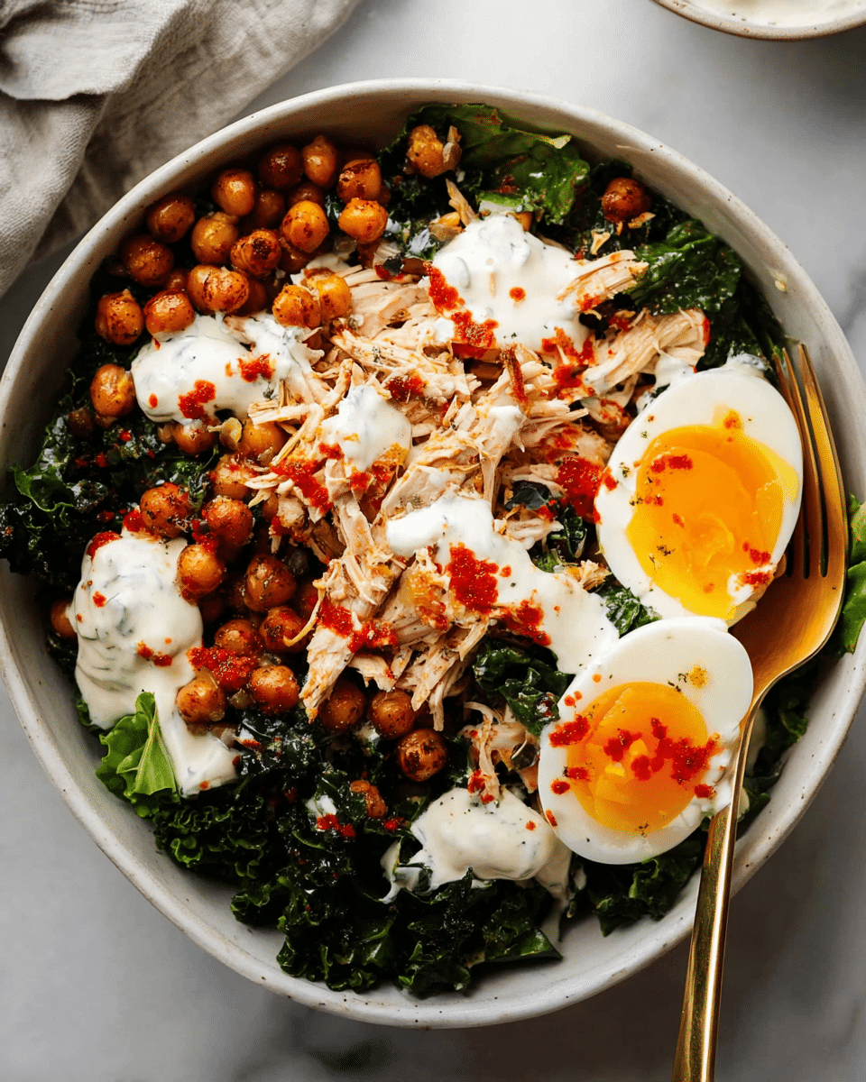A bowl filled with layers starting from the base of dark green kale leaves, topped with light brown shredded chicken pieces spread evenly, followed by golden roasted chickpeas scattered on top. On one side of the bowl, two halves of a soft boiled egg with bright orange yolks are placed. There are dollops of creamy white dressing drizzled across the ingredients, with small patches of red sauce adding color contrast. The bowl is white, sitting on a white marbled surface, with a gold spoon resting inside. Photo taken with an iphone --ar 4:5 --v 7