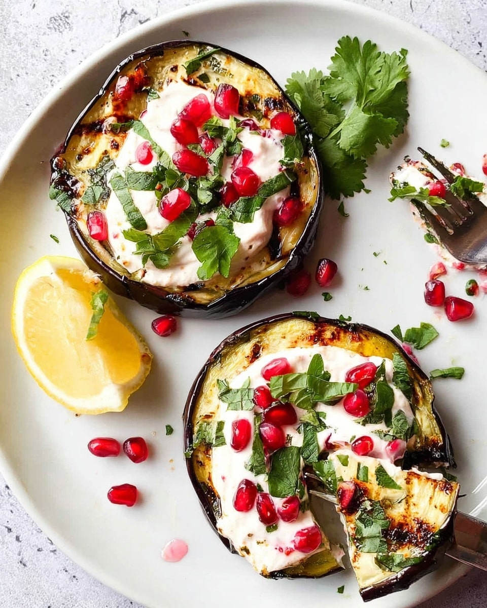 The image shows two round grilled eggplant slices on a white plate with a white marbled texture background. Each eggplant slice has three layers: a dark purple and charred outer edge, a soft golden-brown grilled inside, and a thick white creamy topping spread evenly on top. The creamy layer is decorated with small, bright red chili slices, scattered pomegranate seeds, and fresh green cilantro leaves. There are two lemon wedges on the side of the plate, and one eggplant slice is partly cut with a fork lifting a piece that shows the layers clearly. Photo taken with an iphone --ar 4:5 --v 7