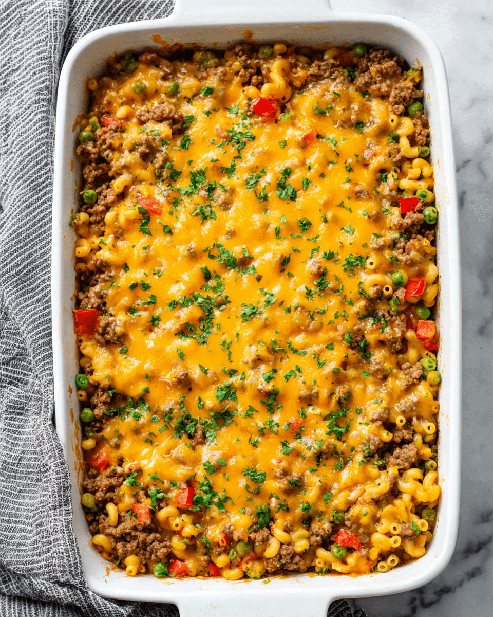 A white rectangular baking dish filled with a baked casserole showing three visible layers: the bottom layer is a mix of ground beef and cooked elbow macaroni with small pieces of green peas and diced red bell peppers, the middle layer consists of melted golden cheddar cheese evenly spread across the top, and the top layer is sprinkled with fresh chopped green herbs for color contrast, everything resting on a white marbled surface with a striped gray cloth partially visible on the side, photo taken with an iphone --ar 4:5 --v 7