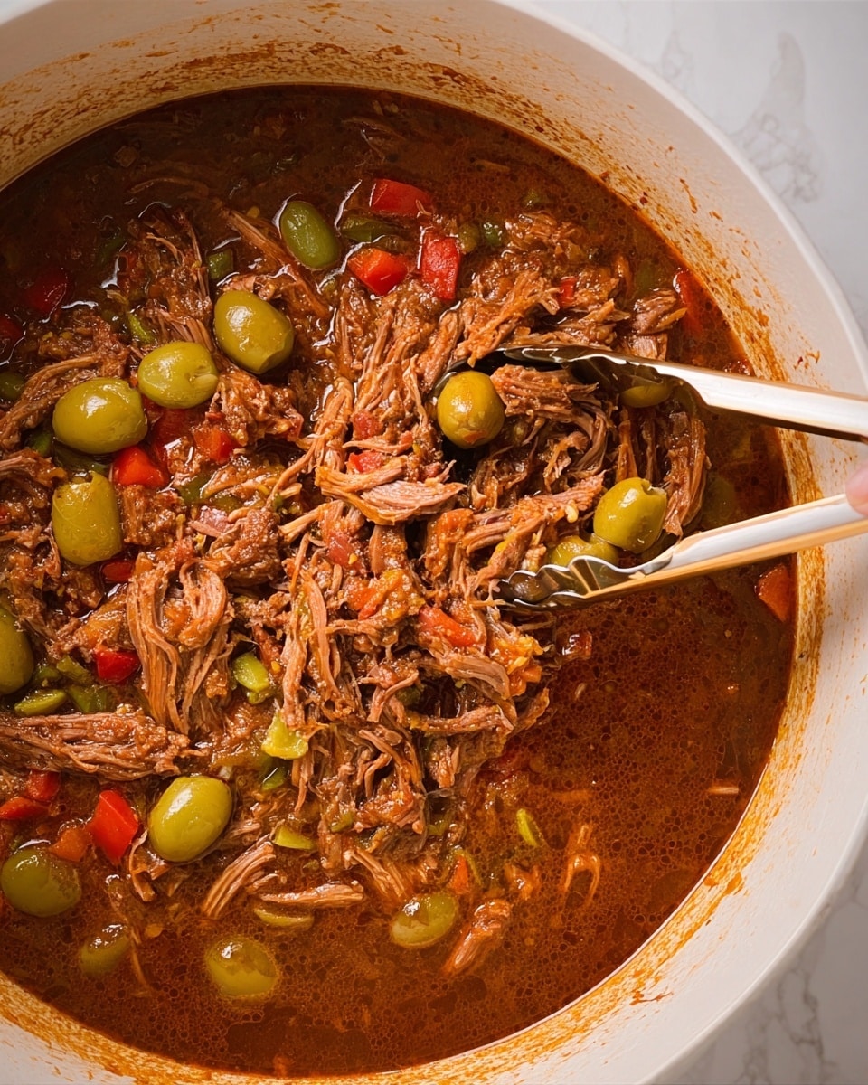 The image shows a white pot filled with shredded meat soaked in a rich, brownish-red sauce. The meat strands have a soft, tender texture, mixed with diced green and red peppers and whole green olives scattered across the dish. Two white and gold tongs are held by a woman's hand, lifting some of the shredded meat from the thick, juicy sauce. The pot's interior is white, contrasting with the dark, vibrant colors of the meat and vegetables inside. The surface beneath the pot has a white marbled texture. photo taken with an iphone --ar 4:5 --v 7