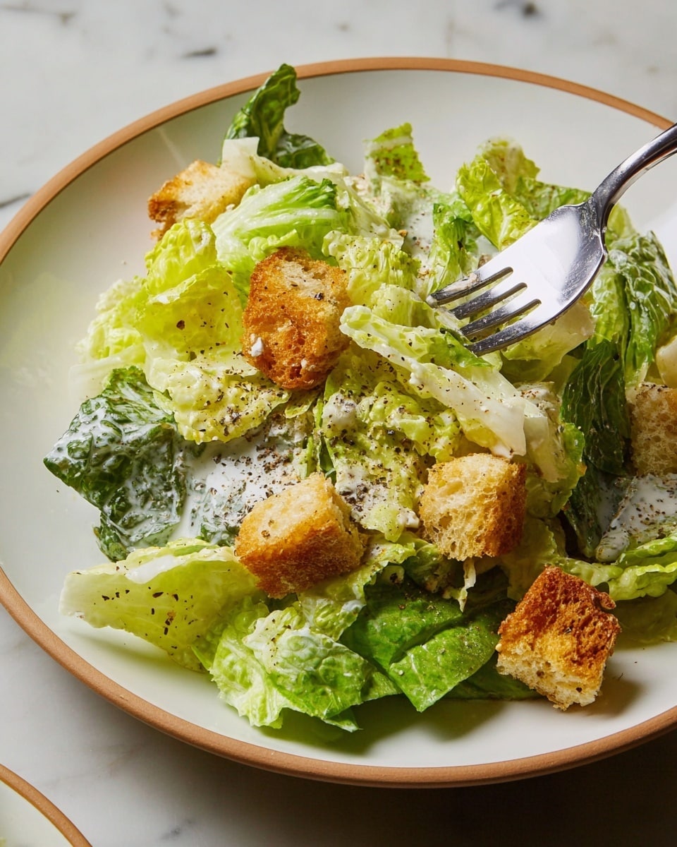 A white plate shows a fresh Caesar salad with three main layers: at the bottom, dark green lettuce leaves; the middle layer has creamy light green lettuce pieces coated with white dressing; on top there are golden brown crunchy croutons sprinkled with black pepper. A silver fork pierces some light green lettuce near the center, and the plate sits on a white marbled surface. photo taken with an iphone --ar 4:5 --v 7