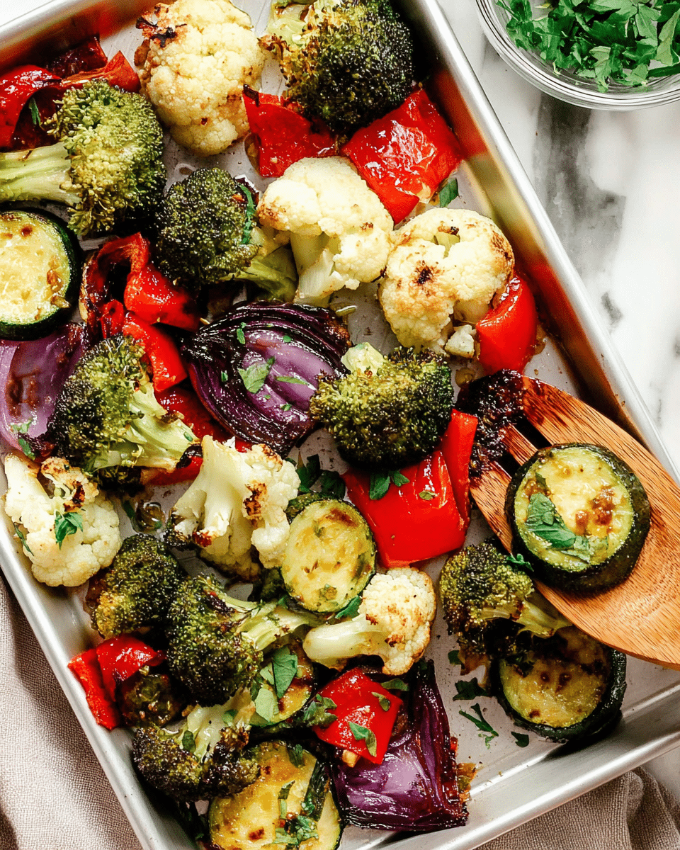 A white tray filled with roasted vegetables including green broccoli florets with slightly charred edges, creamy white cauliflower pieces with golden-brown spots, bright red bell pepper chunks that look soft and wrinkled, thick slices of round green zucchini with browned grill marks, and purple onion segments that appear cooked and shiny. The vegetables are sprinkled with small green herb leaves, and a wooden spatula is lifting some of the veggies. The tray is set on a white marbled surface with a small portion of a bowl containing green leafy herbs visible on the side. Photo taken with an iphone --ar 4:5 --v 7