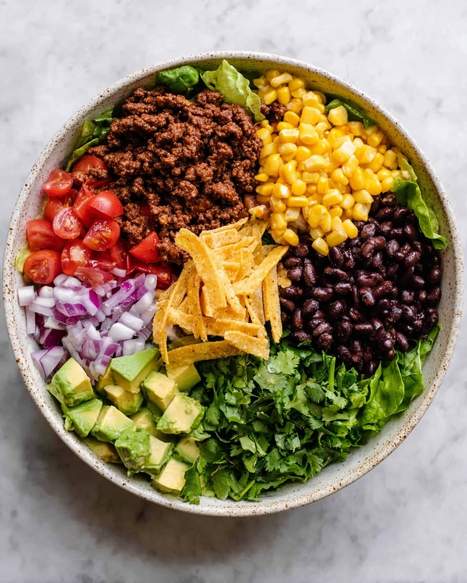 A large white speckled bowl is filled with a mixed salad showing layers of fresh green leafy lettuce, chopped red tomatoes, diced avocado, yellow corn kernels, black beans, and small pieces of cooked ground beef. Finely chopped red onion and thin strips of crispy tortilla chips are spread evenly throughout. On top, two bright green lime wedges rest as garnish. Two rustic wooden salad spoons sit inside the bowl, partially submerged in the salad. The bowl is placed on a white marbled surface with some blurred green leaves and a red object in the background. Photo taken with an iphone --ar 4:5 --v 7