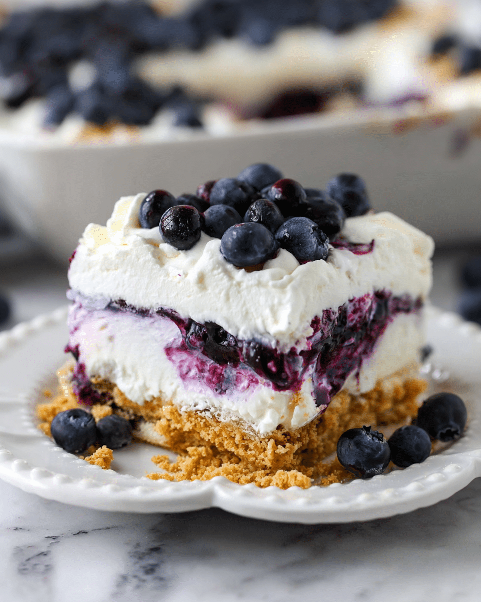 A square slice of blueberry dessert with four clear layers sits on a white scalloped plate over a white marbled surface. The bottom layer is crumbly and golden brown, like crushed graham crackers. Above that, a thick cream layer with swirls of dark purple blueberry filling creates a mix of creamy white and deep purple. The third layer is fluffy and white, topped with a smooth white whipped cream layer. Fresh, whole blueberries are scattered on top and around the plate, adding rich blue color and texture. In the blurred background, a larger dish shows the rest of the dessert with more blueberries on top. photo taken with an iphone --ar 4:5 --v 7