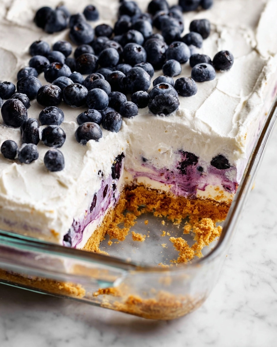 This dessert in a clear glass square dish has three main layers: the bottom layer is a thick, crumbly golden-brown crust, the middle layer is a purple and white creamy mix with blueberry swirls, and the top layer is smooth white whipped cream spread evenly. Fresh whole blueberries are scattered over the top cream layer, adding dark blue spots. A corner piece has been removed, showing the layers clearly. The dish is placed on a white marbled surface. photo taken with an iphone --ar 4:5 --v 7