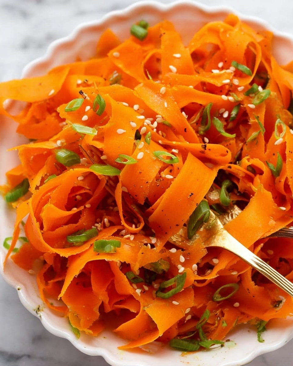 A close-up of a white bowl filled with thin, wide ribbons of bright orange carrot strips, some twisted and curled, topped with small bits of green chopped scallions scattered throughout. White sesame seeds are sprinkled evenly over the carrot ribbons, adding small textured dots. A gold fork is partially buried among the carrot strips, with its prongs holding a small bundle of the ribbons. The dish sits on a white marbled surface. photo taken with an iphone --ar 4:5 --v 7