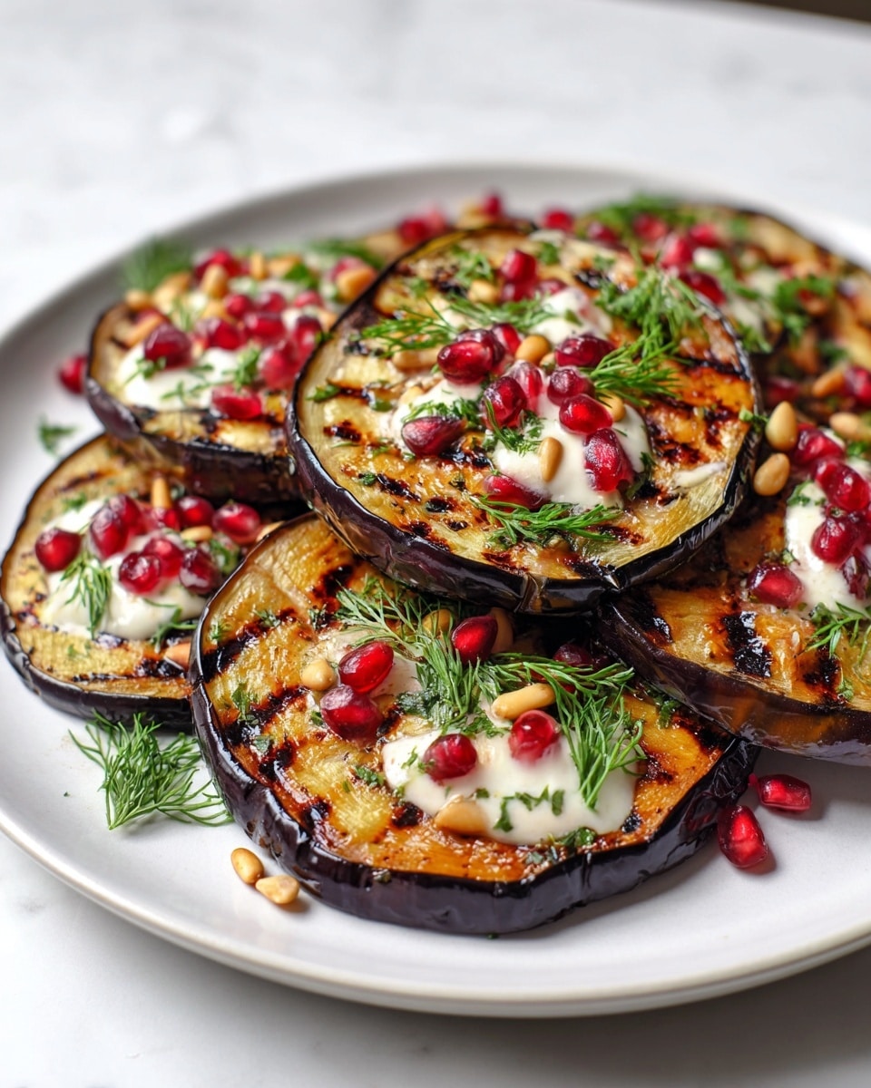 A white plate holds several thick, round slices of grilled eggplant with dark purple edges and a charred, deep orange center that shows clear grill marks. The slices are layered slightly overlapping each other in a casual pile. On top of the eggplant are small dollops of creamy white sauce, bright red pomegranate seeds, light beige pine nuts, and finely chopped green herbs, with some sprigs of fresh dill scattered around for garnish. The plate sits on a white marbled surface. photo taken with an iphone --ar 4:5 --v 7