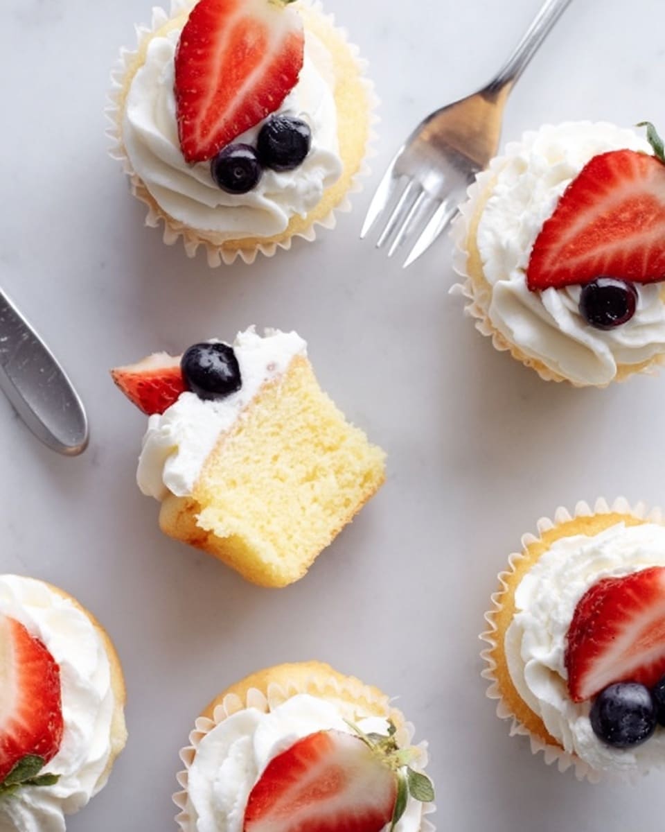 The image shows six small cupcakes placed on a white marbled surface. Each cupcake has a golden-yellow base with a soft, fluffy texture, topped with a swirl of smooth white cream. On top of the cream, fresh fruit slices add color: three have bright red strawberry halves, and two have small clusters of dark blueberries. One cupcake is cut in half, with its light yellow cake and white cream clearly visible in layers, and one silver fork lies beside it. The overall look is clean and fresh with soft, pastel tones. photo taken with an iphone --ar 4:5 --v 7