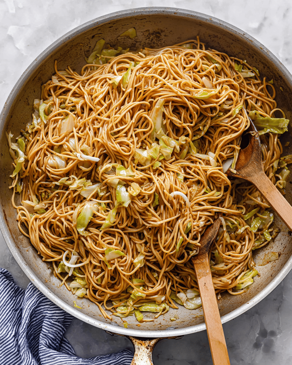 A large metal pan filled with stir-fried noodles mixed with small pieces of light green and pale yellow cabbage. The noodles are a light brown color, neatly tangled and coated with sauce, showing a slightly shiny texture. Two wooden spoons are positioned inside the pan, one lifting some noodles towards the center, showing thin round strands and bits of cabbage. The surface under the pan is white with a marbled pattern, and a blue and white striped cloth is partly visible on the bottom left. The scene looks bright and fresh, focused closely on the food. photo taken with an iphone --ar 4:5 --v 7