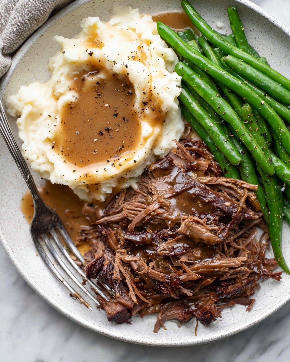 A white plate with three main layers of food: on the top left is a creamy white mashed potato layer with smooth, soft texture, topped with light brown gravy and small specks of black pepper; on the top right, bright green, shiny green beans are laid out in a tight bunch, sprinkled lightly with black pepper; on the bottom half, there is a thick layer of shredded dark brown pot roast with visible juicy strands and some chunks, covered lightly by brown gravy with flecks of black pepper, a metal fork is placed on the bottom right touching the pot roast; the whole plate sits on a white marbled surface. photo taken with an iphone --ar 4:5 --v 7