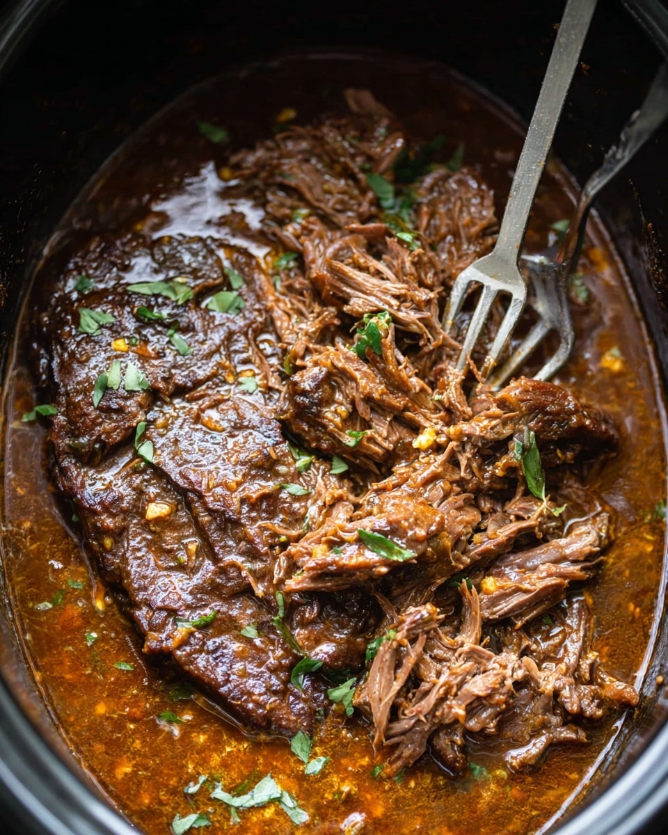 A close-up top view of a pot filled with cooked beef in a rich brown sauce, showing two main layers: the beef itself and the sauce. The beef covers most of the pot, with one part whole and browned with visible texture and slight char, and another part shredded into fibrous pieces. The sauce is thick, glossy, and brown with some orange oil sheen, surrounding the beef and pooling at the edges. Small green herb leaves are scattered on top for garnish. A long metal fork with two prongs is stuck into the shredded beef, pulling it apart. The background inside the pot is dark, highlighting the colors and textures of the beef and sauce. Photo taken with an iphone --ar 4:5 --v 7