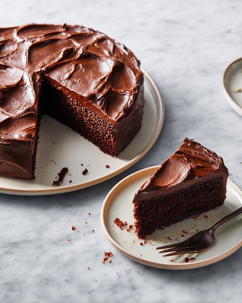 A round chocolate cake with thick, glossy dark chocolate frosting spread unevenly on top, creating smooth swirls and textured peaks. One large slice is cut and placed on a smaller white plate to the right, showing the cake’s moist, dark brown inside layer beneath the shiny frosting layer. There are small crumbs scattered around the plates. A dark bronze fork rests next to the slice on the smaller plate. The background is a white marbled texture. photo taken with an iphone --ar 4:5 --v 7