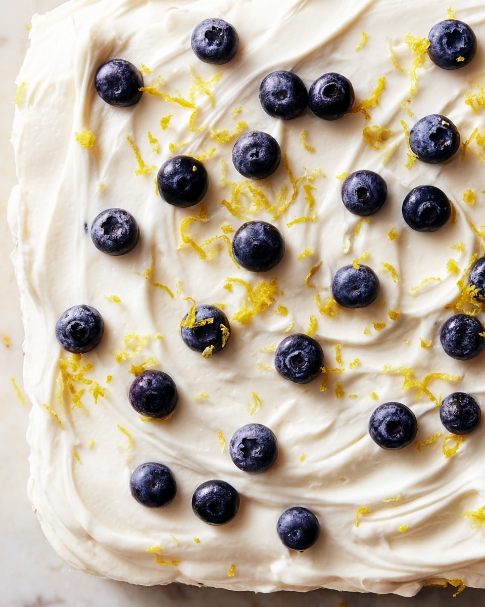A close-up view of a dessert layer showing smooth white cream spread thickly with gentle swirls across the surface. Scattered evenly over the cream are small, round blueberries with deep blue-purple color and a matte texture. Bright yellow lemon zest pieces are sprinkled lightly on top, adding a pop of color and fine texture. The dessert rests on a base that is barely visible at the edges, sitting on a white marbled surface. photo taken with an iphone --ar 4:5 --v 7