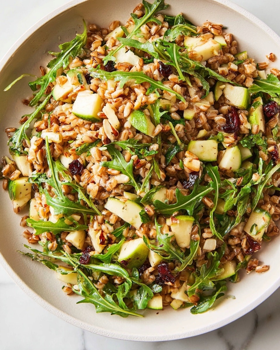 The image shows a close-up of a grain salad in a white bowl, placed on a white marbled surface. The salad has one main layer made of cooked grains, light brown in color with a slightly chewy texture, mixed with small green apple pieces that have a fresh and crisp look. Scattered throughout are bright green arugula leaves, adding a leafy texture and freshness. There are also small bits of nuts and dried cranberries, providing a crunchy and chewy contrast, along with thin, lightly browned onion slices visible near the edges. The overall mix looks fresh and colorful with a mix of earthy and bright tones. Photo taken with an iphone --ar 4:5 --v 7