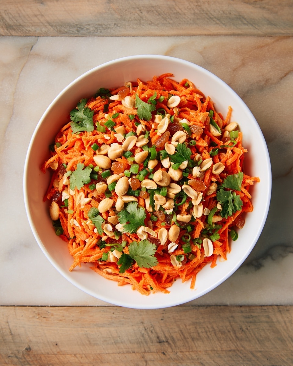 The image shows a close-up of a carrot salad served in a white bowl. The dish has one main layer of bright orange shredded carrots mixed with light green chopped scallions and topped with pale beige peanuts, golden raisins, and fresh green cilantro leaves scattered on top. The textures range from soft shredded carrots to crunchy peanuts and leafy cilantro. The bowl sits on a white marbled surface with a blue and white striped cloth nearby. photo taken with an iphone --ar 4:5 --v 7