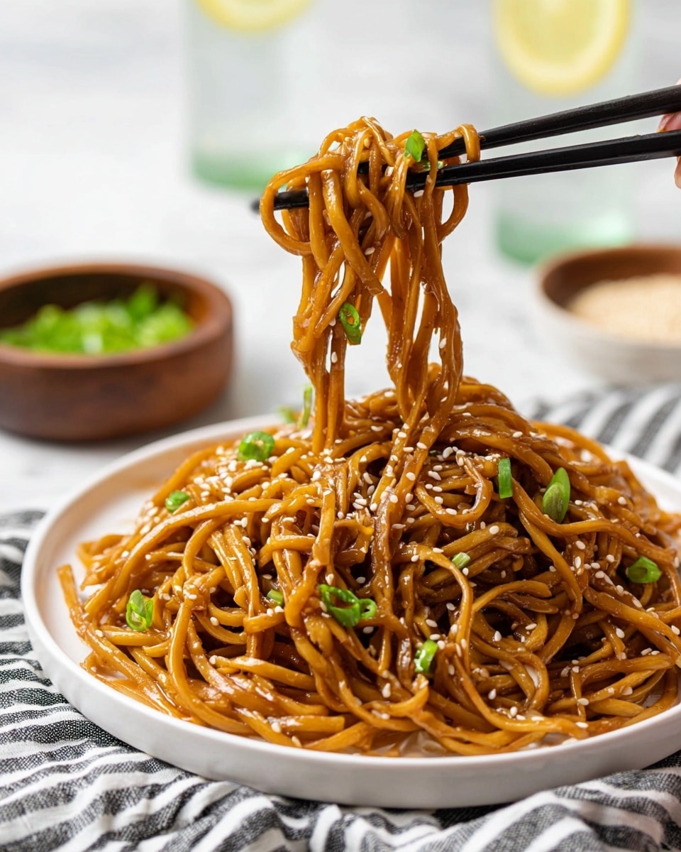 A close-up view of glossy brown noodles coated in sauce, held up by black chopsticks with a woman's hand just out of frame. The noodles are sprinkled with white sesame seeds and chopped green onions, showing their soft and slightly sticky texture. The base layer is a white round plate filled with more noodles, sitting on a cloth with black and white stripes. In the blurred white marbled background, a small white bowl with green onions and a wooden bowl with light sesame seeds are visible, along with two glasses of water with lemon slices. photo taken with an iphone --ar 4:5 --v 7