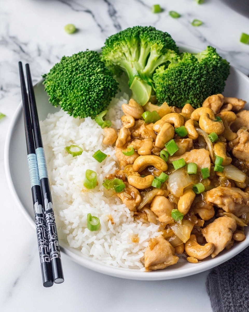 A white plate sits on a white marbled texture, filled with three layers: at the bottom is a bed of fluffy white rice, on top of the rice is a golden-brown stir-fry with pieces of chicken, cashew nuts, and small chunks of light brown onions, all coated with a shiny sauce, garnished with chopped green onions scattered over the stir-fry; on the side of the plate are three large bright green broccoli florets. A pair of black chopsticks with white and blue bands rests on the edge of the plate. Photo taken with an iphone --ar 4:5 --v 7