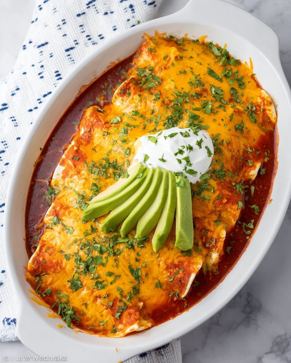 A white oval dish filled with three layers: the bottom layer is dark red sauce, the middle layer consists of folded tortillas soaked in sauce, and the top layer is melted orange cheddar cheese sprinkled with chopped green herbs. On top, there is a dollop of white sour cream with more green herbs and three slices of light green avocado arranged in a fan shape on the edge of the dish. The dish is placed on a white marbled surface next to a white cloth with small blue dots. Photo taken with an iphone --ar 4:5 --v 7