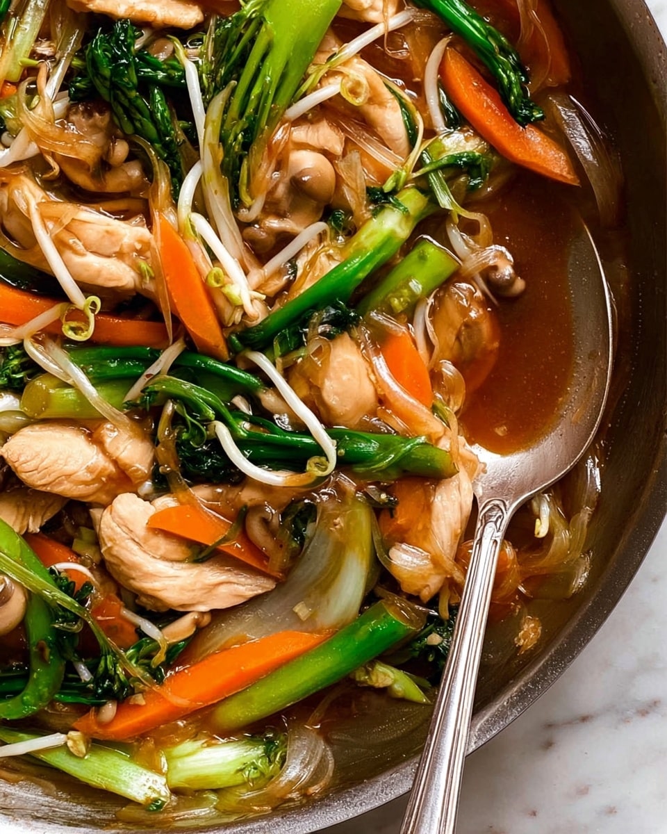 The image shows a close-up of a colorful stir-fry dish in a pan, featuring layers of vibrant ingredients. The base layer includes light brown cooked chicken slices with a tender, slightly glossy texture. Mixed in are bright orange carrot sticks cut into thin strips, fresh green stalks and leaves resembling broccolini or asparagus, and white bean sprouts with soft, translucent stems. Light beige mushroom slices add an earthy texture, all coated in a shiny brown sauce that pools slightly at the bottom. A silver spoon rests on the right side of the pan, partially submerged in the sauce with some vegetables. The background is a white marbled texture. photo taken with an iphone --ar 4:5 --v 7
