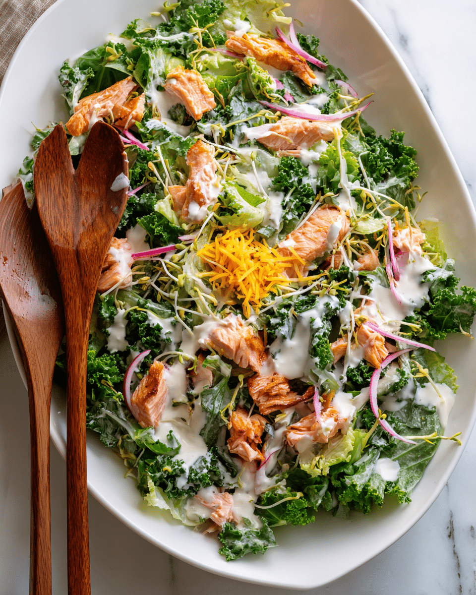 A white oval bowl filled with a colorful layered salad. The bottom layer shows mixed green leaves including kale and lettuce, with a fresh, textured look. Scattered on top are small pieces of cooked salmon, showing a slightly crispy, browned exterior and pink inside. Thin, light green sprout shoots cover much of the salad surface, adding height. There are thin strands of bright pink pickled onions peeking through. A creamy white dressing is drizzled unevenly over the top, slightly pooling in some spots. A small sprinkling of finely shredded pale yellow cheese sits in the center. Two wooden salad tongs rest in the bowl on the left side. The bowl sits on a white marbled textured surface. photo taken with an iphone --ar 4:5 --v 7