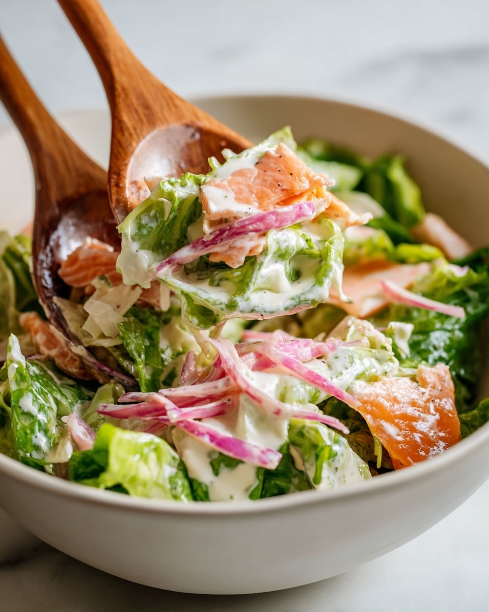 A close-up shot shows a fresh salad being mixed with two wooden spoons inside a white bowl placed on a white marbled surface. The salad has several layers and textures: the base layer is bright green leafy lettuce, combined with thin slices of pink pickled onions and shredded white cheese or coleslaw. There are orange chunks of cooked salmon and light creamy dressing drizzled all over, adding a smooth texture. The wooden spoons lift some salad, showing the mix of creamy, crunchy, and soft parts well blended together. Photo taken with an iphone --ar 4:5 --v 7