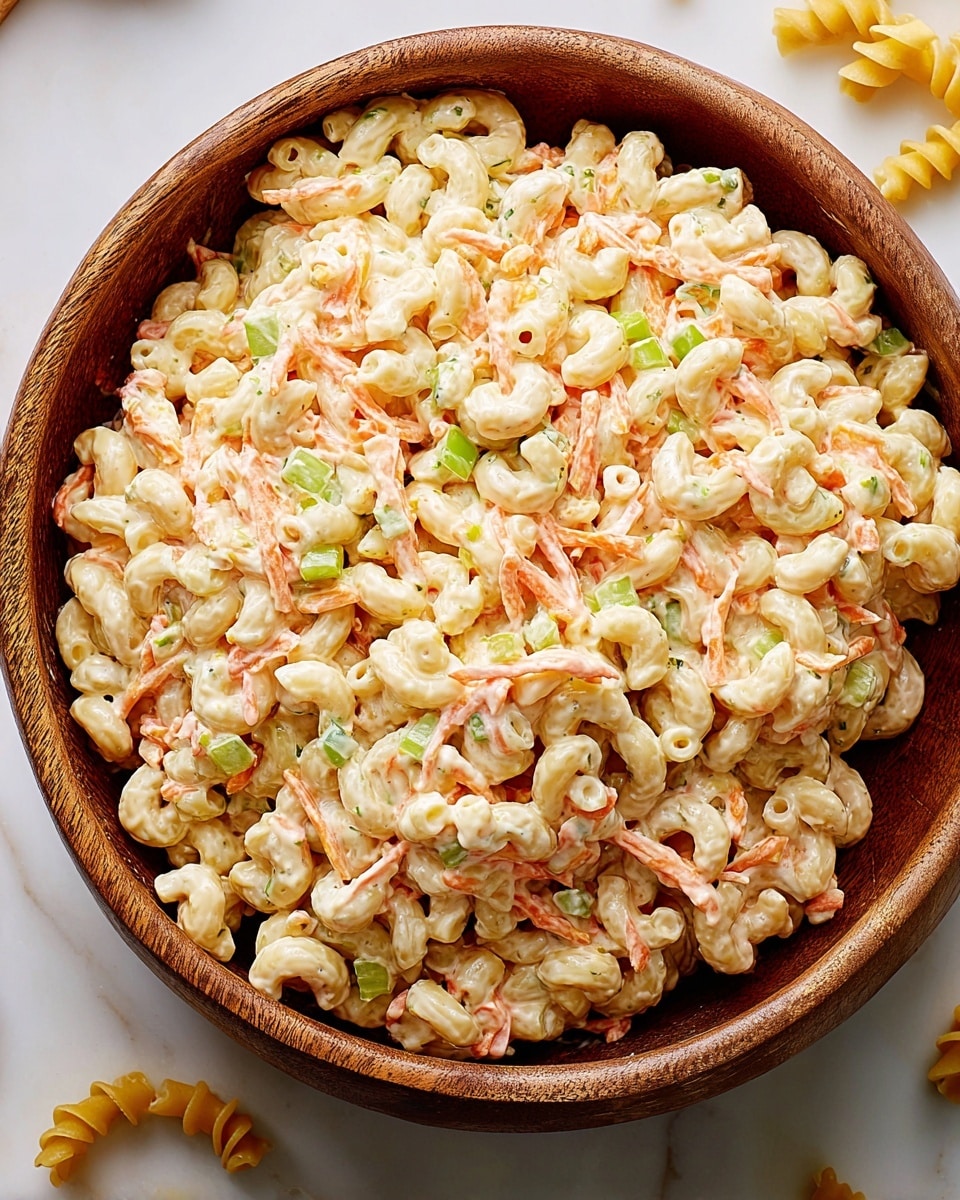 A large wooden bowl filled with creamy macaroni salad made of small, curved pasta mixed with mayonnaise, thin orange carrot strips, and small green celery pieces evenly spread throughout. The creamy texture is thick and coats each ingredient well, with colors mainly light cream from the sauce, pale yellow from the pasta, bright orange from the carrots, and fresh green from the celery bits. The bowl sits on a white marbled surface with a few pasta pieces scattered around it. photo taken with an iphone --ar 4:5 --v 7