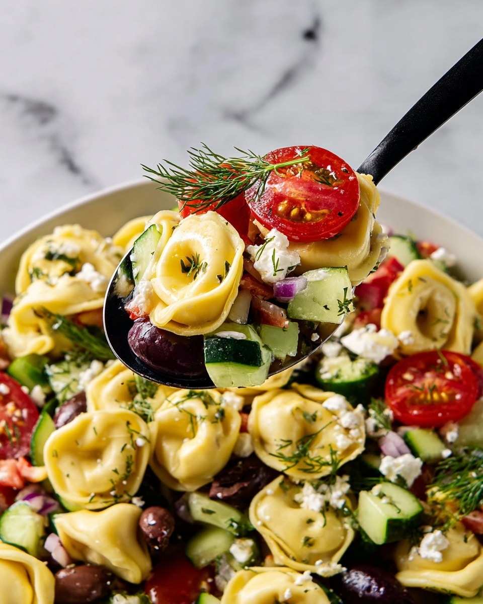 The image shows a close-up of a spoon holding a mix of tortellini pasta, bright red cherry tomato halves, dark purple olives, green cucumber slices, white crumbly cheese, and small green dill sprigs. The tortellini pasta is soft yellow with a smooth texture, forming the base layer, while the tomatoes and cucumbers add fresh, juicy pops of color. The olives add a deep purple contrast, and the cheese crumbles are scattered throughout, adding a white touch. Fresh dill sprigs with thin green needles are spread across the dish for a delicate garnish. The spoon is black, held above a larger pile of the same salad on a white plate, all set on a white marbled surface. Photo taken with an iphone --ar 4:5 --v 7