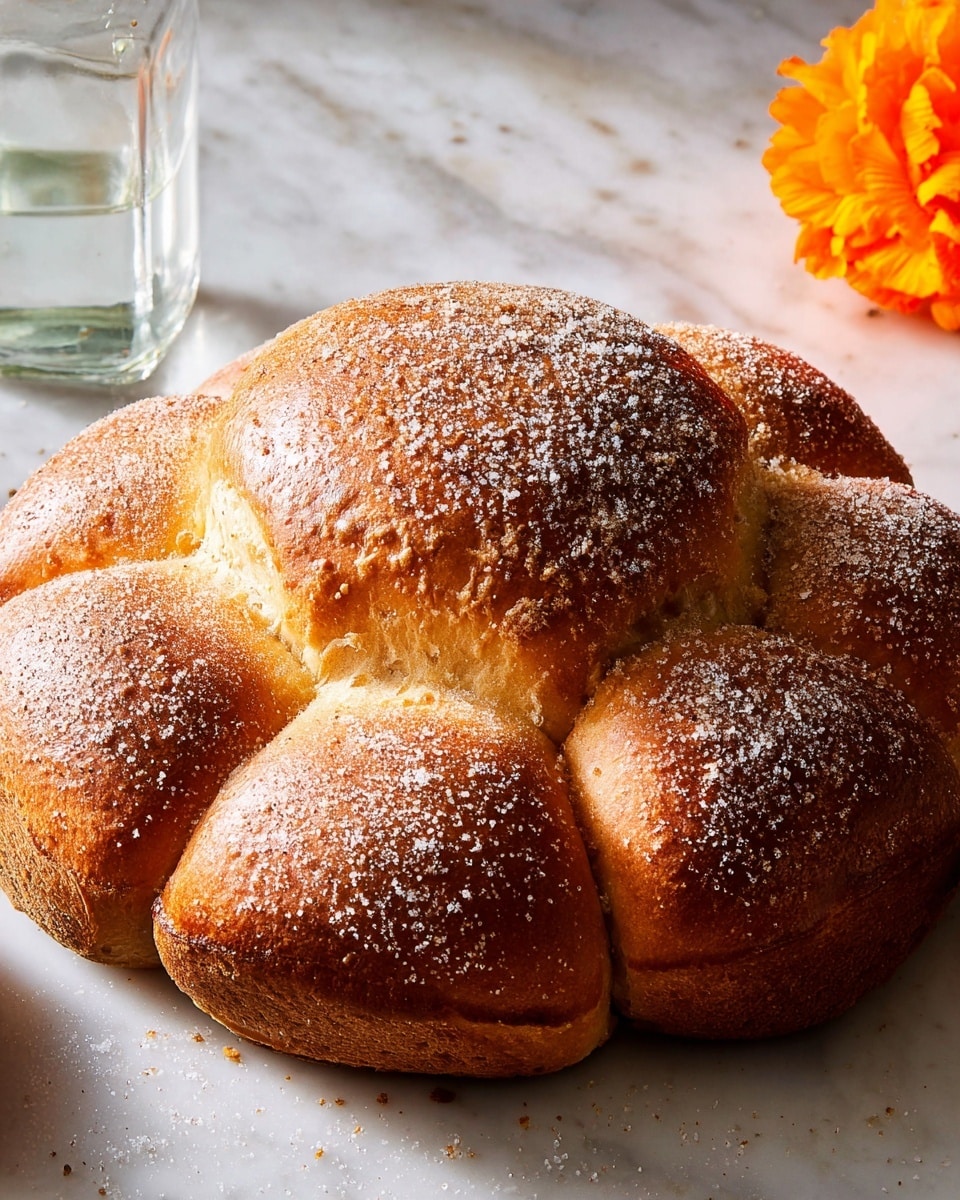 A round bread with five distinct dough sections forming a flower shape, all golden brown with a slightly rough texture on the top crust. The center dome is prominent and rises higher than the four connected smaller domes around it. The outer sections have a dusting of white sugar granules, giving a sparkly effect. The bread sits on a white marbled surface with soft natural light highlighting the sugary crust. A clear glass bottle is in the back left, and a bright orange flower petal cluster is partially visible on the white marbled surface on the right side. Photo taken with an iphone --ar 4:5 --v 7