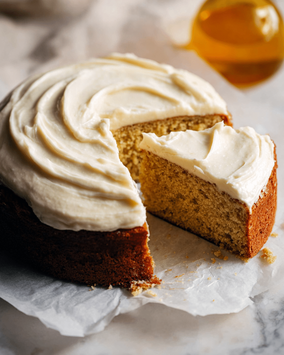 The image shows a round cake with two layers: the bottom layer is golden brown with a slightly textured, moist interior, and the top layer is a thick, creamy white frosting with smooth swirls. One large slice has been cut out, revealing the soft inside of the cake. The cake sits directly on white parchment paper, which rests on a white marbled surface. The background has a blurred glass bottle with a warm yellow color. Photo taken with an iphone --ar 4:5 --v 7