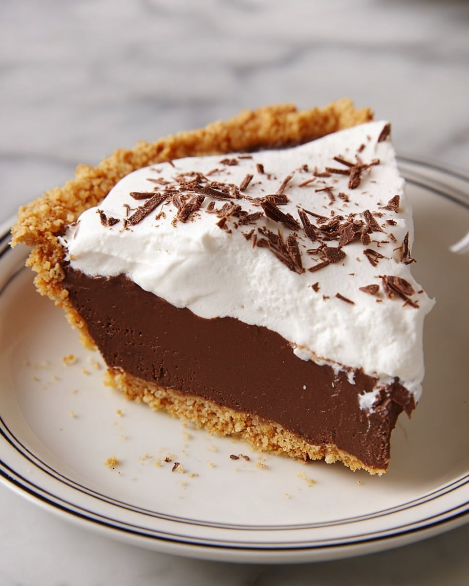 A slice of pie with three distinct layers sits on a white plate with a thin black rim. The bottom crust is crumbly and golden brown, providing a sturdy base. Above it is a thick, smooth dark chocolate layer with a creamy texture. The top layer is a fluffy, white whipped cream spread evenly and sprinkled with small, thin chocolate shavings scattered across the surface. The background is a white marbled surface. photo taken with an iphone --ar 4:5 --v 7