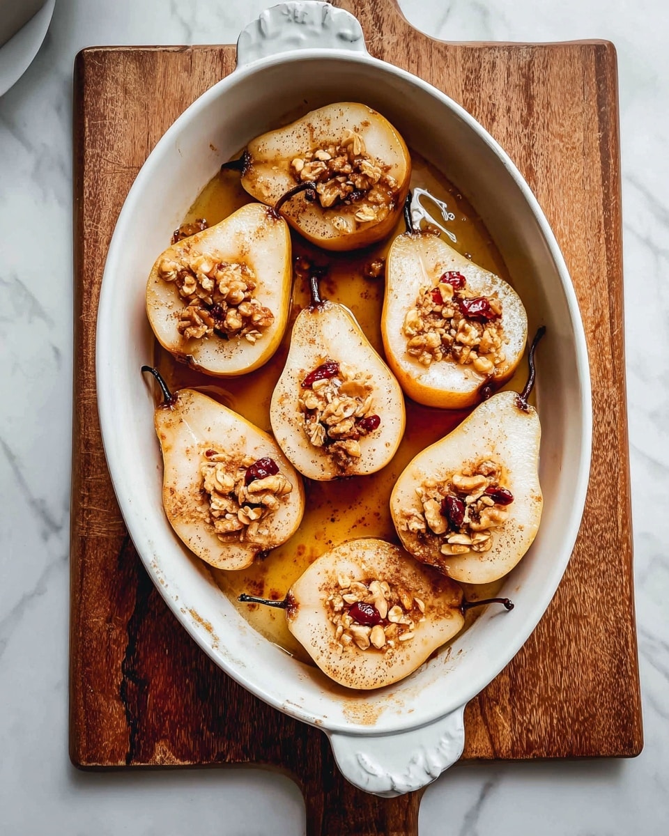 A white oval pan holds eight pear halves arranged closely, each pear cut in half lengthwise with the core scooped out. The pears are light cream with soft brown edges from baking, and the centers are filled with granola pieces that show small nuts and dried red berries. A sticky golden brown syrup pools gently around the pears, giving a warm shine and some light cinnamon powder sprinkled on top. The pan rests on a wooden board placed on a white marbled surface, with soft natural light highlighting the textures and colors. photo taken with an iphone --ar 4:5 --v 7