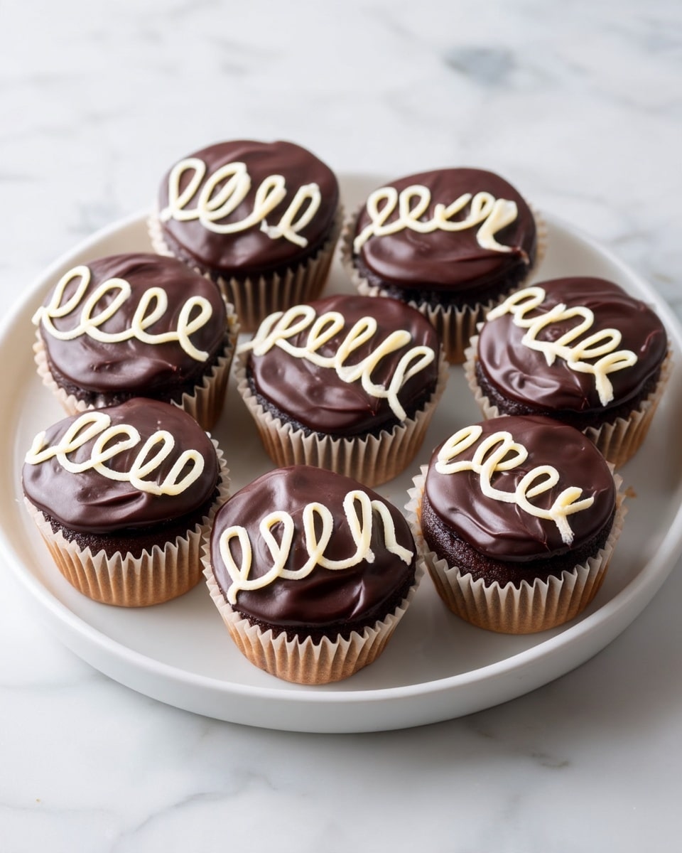 The image shows a white plate filled with chocolate cupcakes, each cupcake having a smooth, glossy layer of dark chocolate frosting on top. Over the dark chocolate frosting on each cupcake, there is a light cream-colored icing swirl design, shaped like a loose zigzag or wave. Each cupcake is wrapped in a light tan paper liner. The cupcakes are arranged evenly on the white plate, which sits on a white marbled surface. photo taken with an iphone --ar 4:5 --v 7