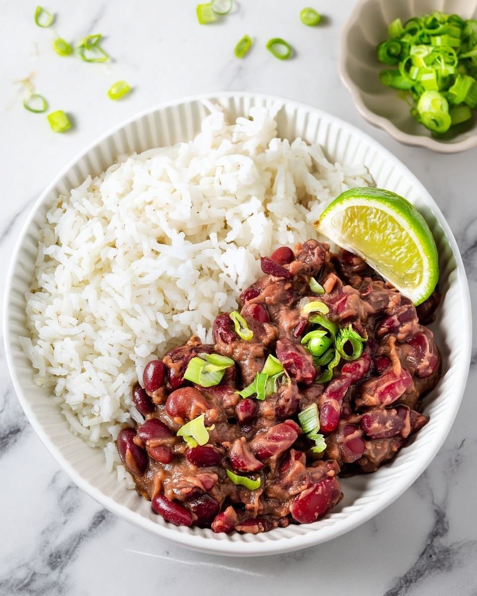 A white bowl holds a serving of cooked white rice on the left side with fluffy, separate grains. On the right side, there is a thick layer of dark red kidney beans in a creamy brown sauce, topped with thinly sliced green onions scattered across it. A bright green lime wedge sits on the top right edge of the beans. The bowl is placed on a white marbled surface with a small dish containing extra green onions nearby. photo taken with an iphone --ar 4:5 --v 7