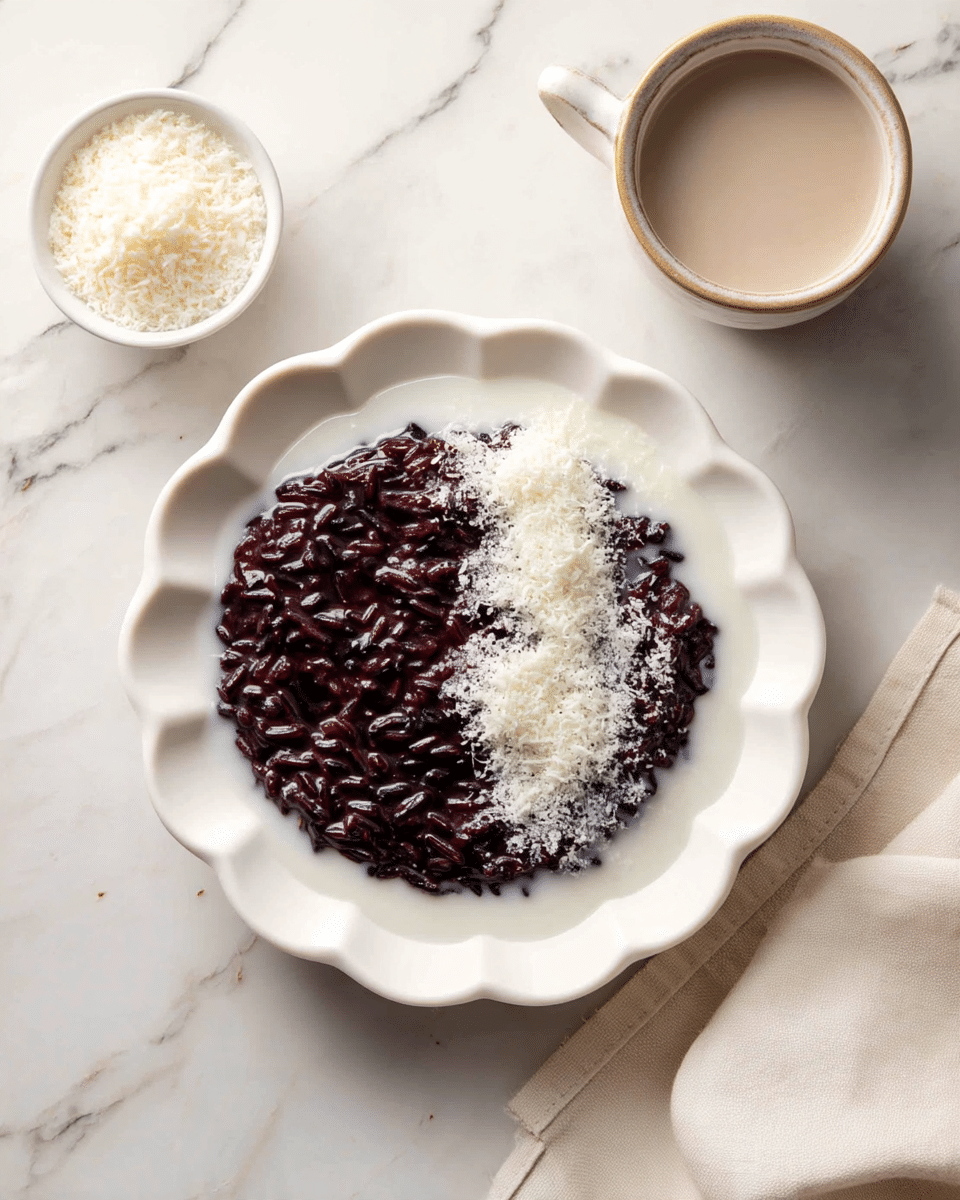 A white scalloped plate holds a dark purple creamy mixture of black rice pudding, with visible whole grains providing texture. A pool of white coconut milk spreads over half of the pudding, creating a smooth contrast with the dark layer beneath. On top of the pudding, there is a sprinkle of fine white shredded coconut adding a textured accent near the right side. The dish rests on a white marbled surface, with a small white bowl of more shredded coconut and a cup of coconut milk nearby, along with a beige cloth napkin at the bottom right corner. Photo taken with an iphone --ar 4:5 --v 7