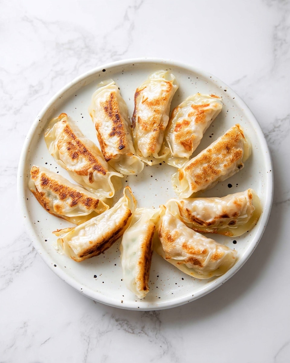 A white ceramic plate with slight speckles holds ten pan-fried dumplings arranged in a loose circular shape. Each dumpling has a semi-translucent dough wrapper showing a hint of the filling inside, with the bottom side golden brown and crispy from frying. The tops of the dumplings are soft and slightly shiny, with uneven pleats and folds. The plate is set on a white marbled surface, creating a clean and light background. photo taken with an iphone --ar 4:5 --v 7